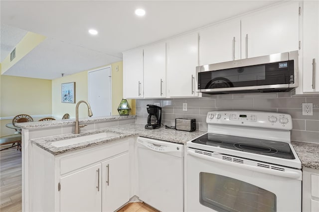 kitchen with a peninsula, white appliances, white cabinets, and a sink