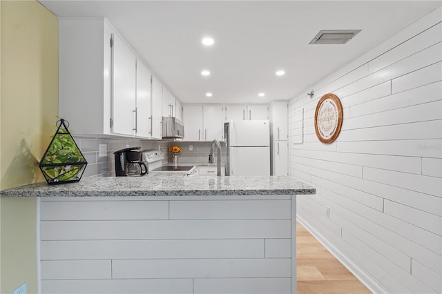 kitchen featuring freestanding refrigerator, white cabinetry, a peninsula, and stove