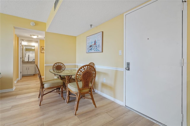 dining area featuring a textured ceiling, light wood-style flooring, and baseboards