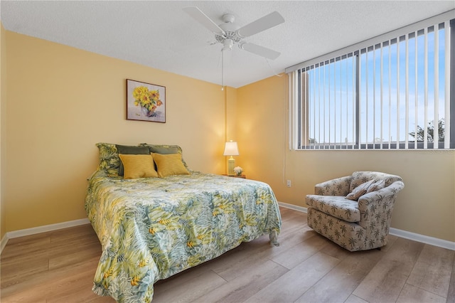 bedroom with ceiling fan, a textured ceiling, baseboards, and wood finished floors