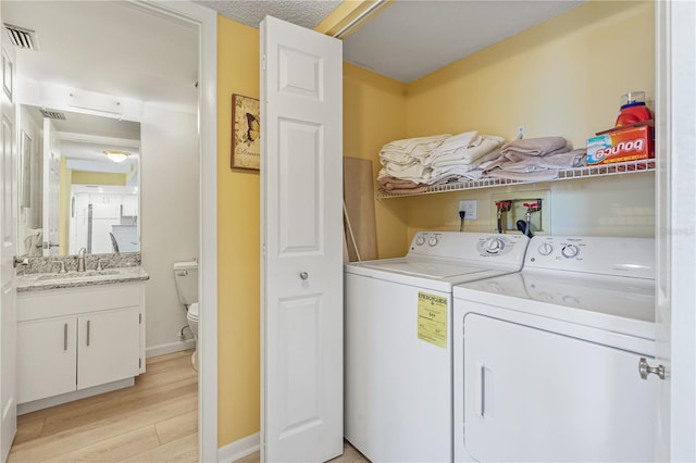 laundry area with visible vents, light wood-style flooring, a sink, separate washer and dryer, and laundry area