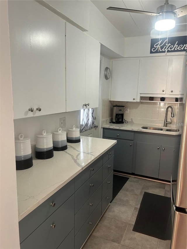 kitchen featuring decorative backsplash, sink, light stone countertops, light tile patterned floors, and white cabinetry