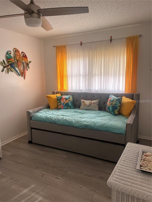 living room with baseboards, a textured ceiling, a ceiling fan, and wood finished floors