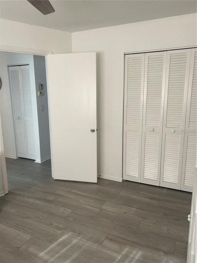 unfurnished bedroom with a closet, baseboards, a textured ceiling, and dark wood-style floors