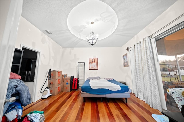 bedroom with hardwood / wood-style flooring, a textured ceiling, a raised ceiling, and a chandelier