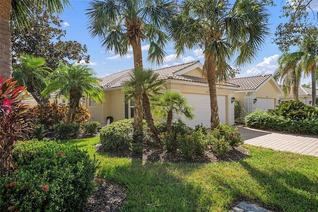 view of front of house with an attached garage, a tiled roof, decorative driveway, stucco siding, and a front lawn