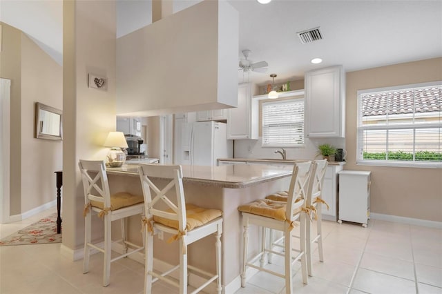 kitchen featuring light tile patterned flooring, white cabinetry, a breakfast bar, ceiling fan, and white fridge with ice dispenser