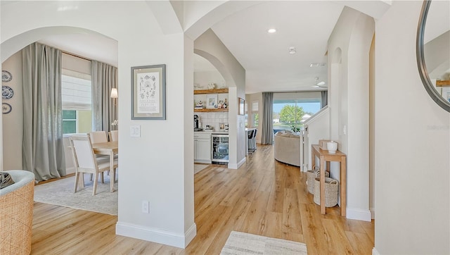 corridor featuring light hardwood / wood-style flooring, beverage cooler, plenty of natural light, and vaulted ceiling