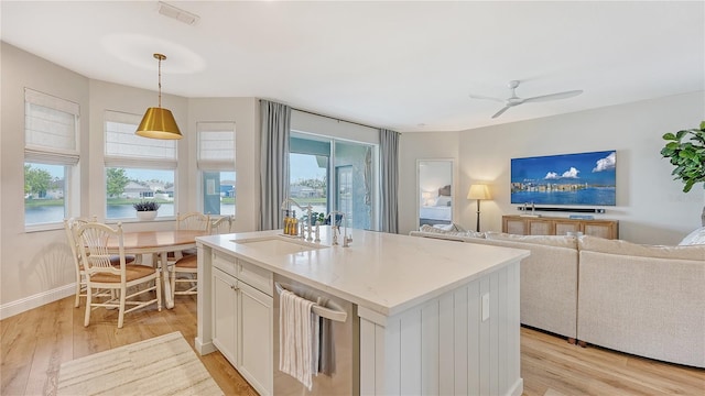 kitchen with a wealth of natural light, an island with sink, hanging light fixtures, and light wood-type flooring