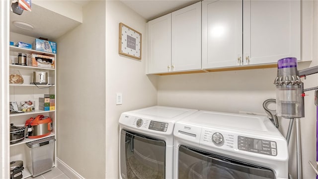 laundry room with washing machine and clothes dryer, light tile patterned floors, and cabinets