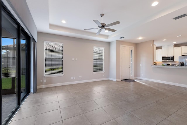 unfurnished living room with ceiling fan, light tile patterned floors, and a tray ceiling