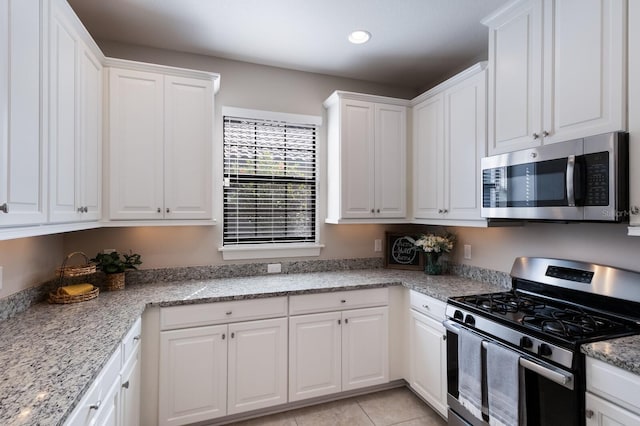 kitchen with light stone countertops, white cabinets, stainless steel appliances, and light tile patterned floors