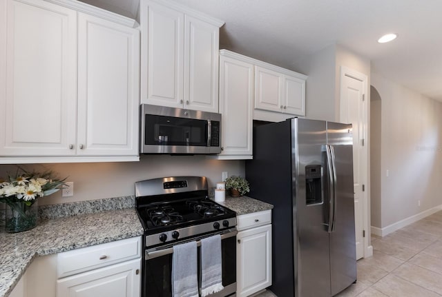 kitchen with white cabinets, light tile patterned floors, stainless steel appliances, and light stone countertops