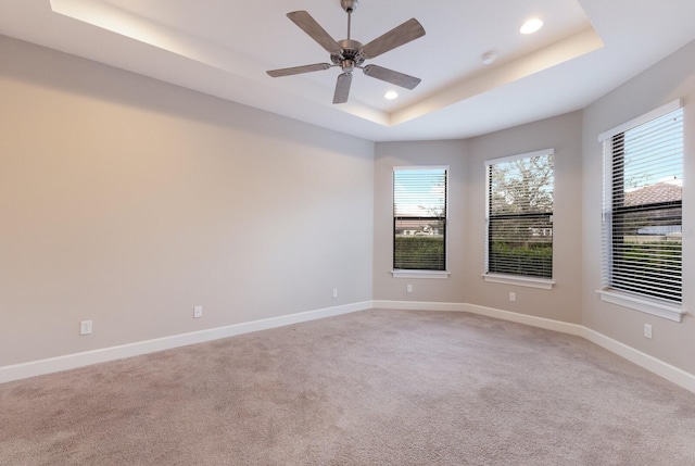 carpeted spare room featuring a tray ceiling and ceiling fan