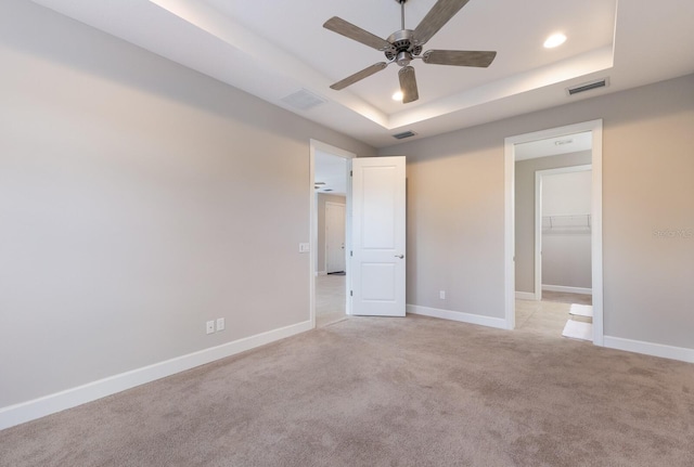 unfurnished bedroom featuring a closet, a walk in closet, a tray ceiling, and ceiling fan