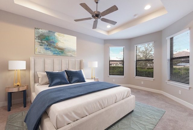 bedroom with light colored carpet, a raised ceiling, and ceiling fan