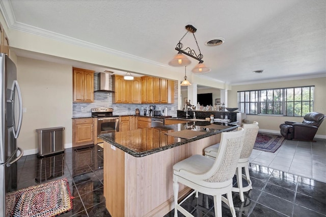 kitchen featuring wall chimney range hood, kitchen peninsula, stainless steel appliances, ornamental molding, and decorative light fixtures