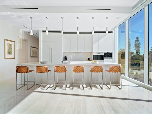 kitchen with sink, an island with sink, a breakfast bar, white cabinetry, and decorative light fixtures