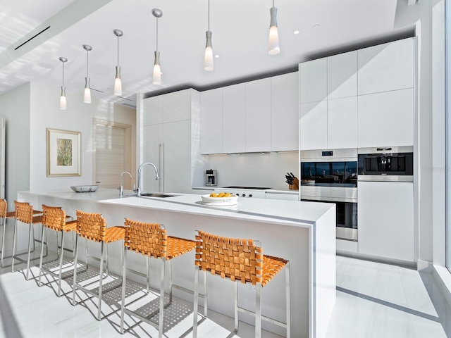 kitchen with hanging light fixtures, a breakfast bar area, white cabinetry, and sink