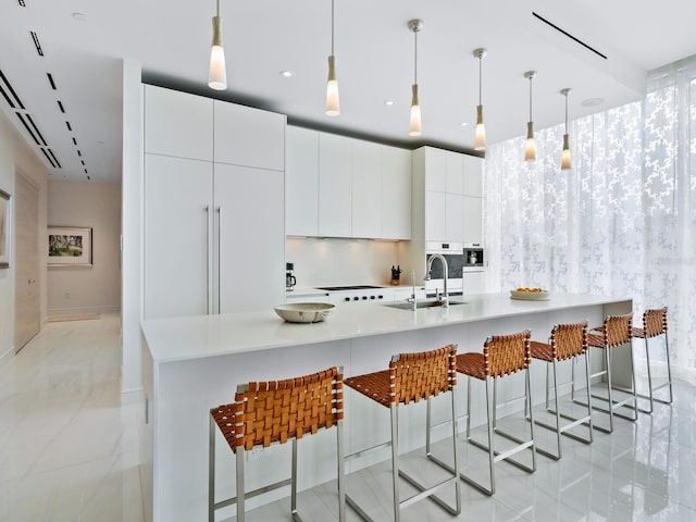 kitchen with a breakfast bar, white cabinetry, sink, and pendant lighting