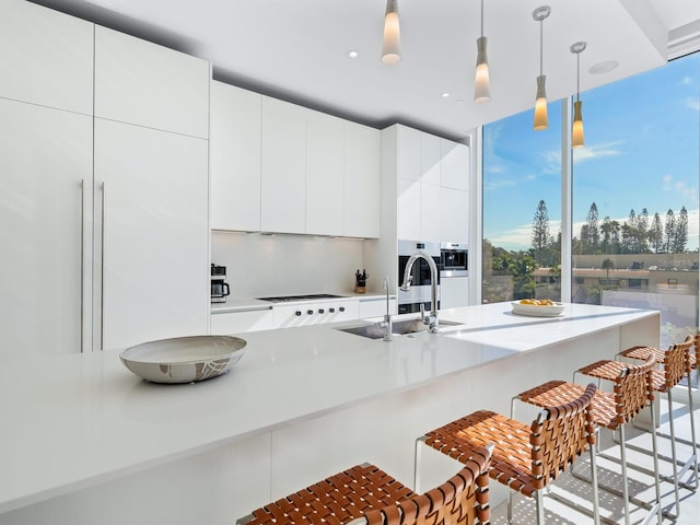 kitchen with cooktop, decorative light fixtures, sink, a breakfast bar, and white cabinets