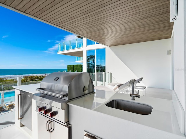 view of patio / terrace featuring area for grilling, a beach view, an outdoor kitchen, sink, and a water view