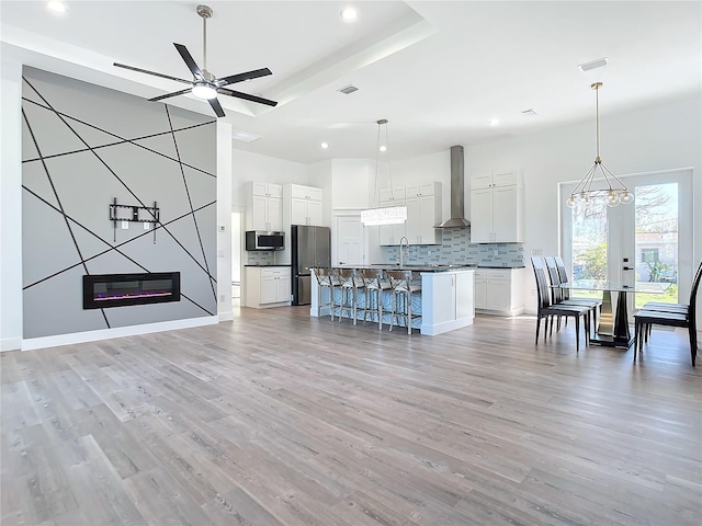 kitchen featuring white cabinetry, stainless steel appliances, wall chimney exhaust hood, light hardwood / wood-style flooring, and a kitchen island with sink