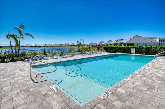 community pool featuring a patio area, a water view, fence, and a residential view