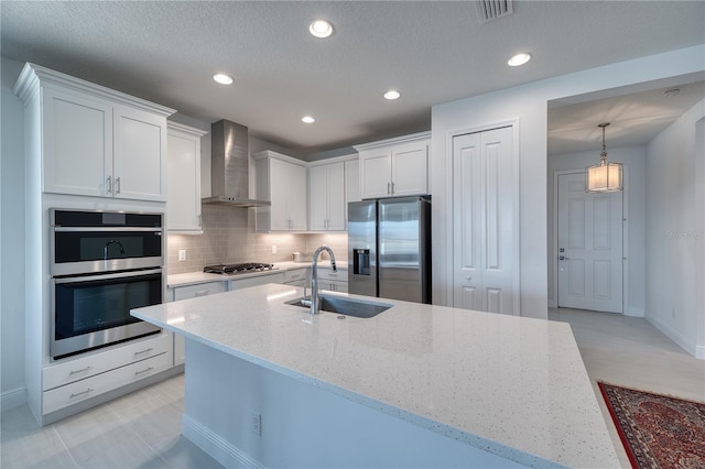 kitchen featuring appliances with stainless steel finishes, white cabinets, a sink, and wall chimney exhaust hood