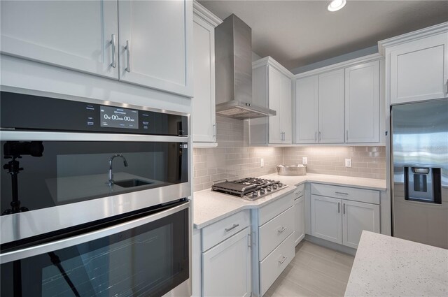 kitchen featuring appliances with stainless steel finishes, backsplash, white cabinets, and wall chimney range hood