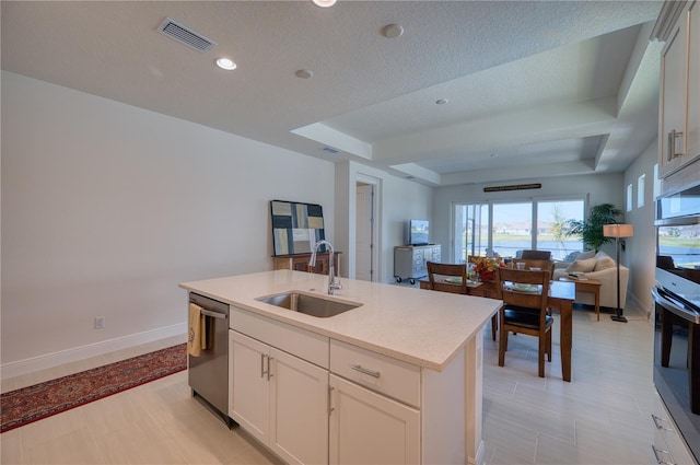 kitchen featuring a center island with sink, light countertops, open floor plan, a sink, and dishwasher