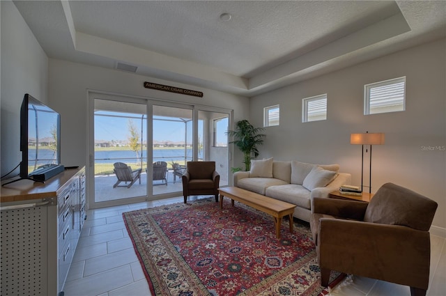 living area with a water view, visible vents, a tray ceiling, and a textured ceiling