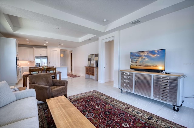 living room featuring light tile patterned flooring, a raised ceiling, visible vents, and baseboards