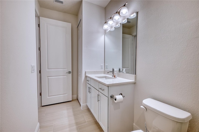 bathroom featuring visible vents, a textured wall, toilet, vanity, and baseboards