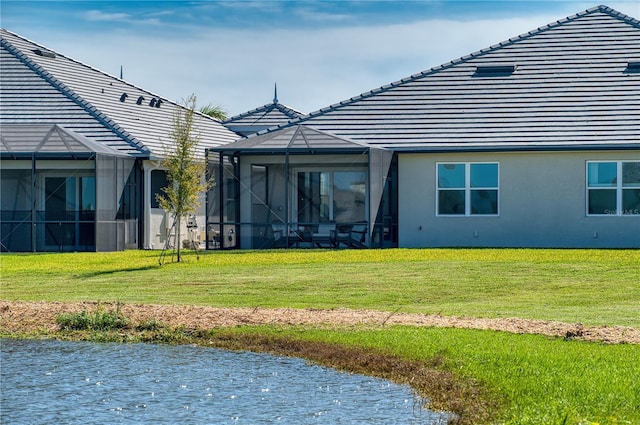 rear view of property with glass enclosure, a tile roof, a lawn, and stucco siding