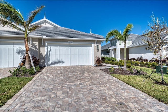 ranch-style home featuring an attached garage, a tiled roof, decorative driveway, and stucco siding