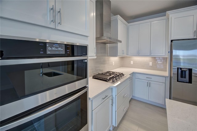 kitchen featuring stainless steel appliances, white cabinets, wall chimney exhaust hood, and light stone countertops