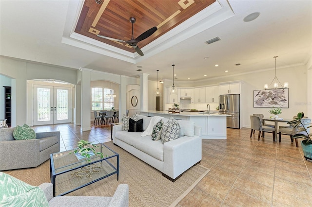 tiled living room featuring ceiling fan with notable chandelier, a raised ceiling, ornamental molding, and french doors