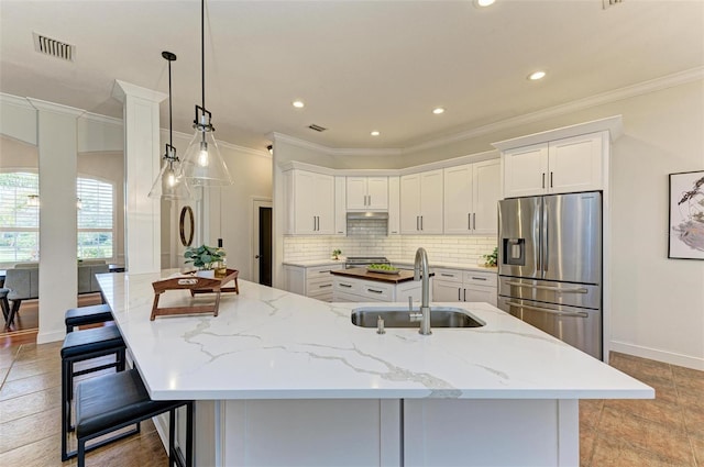 kitchen featuring a kitchen island with sink, white cabinets, sink, stainless steel refrigerator with ice dispenser, and light stone countertops