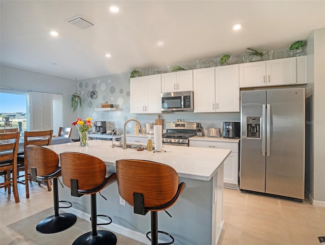 kitchen featuring appliances with stainless steel finishes, white cabinets, sink, an island with sink, and a breakfast bar area