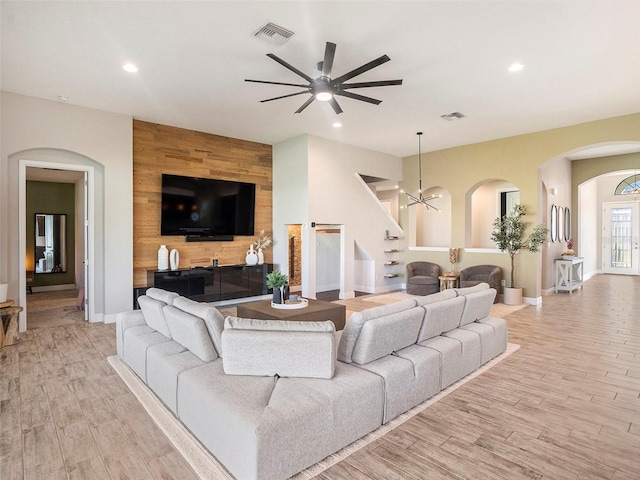 living room featuring ceiling fan with notable chandelier and light hardwood / wood-style flooring