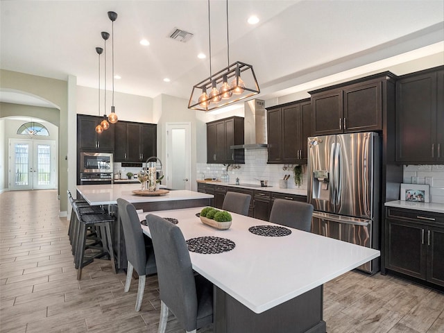 kitchen with a center island with sink, stainless steel appliances, pendant lighting, a breakfast bar area, and wall chimney exhaust hood