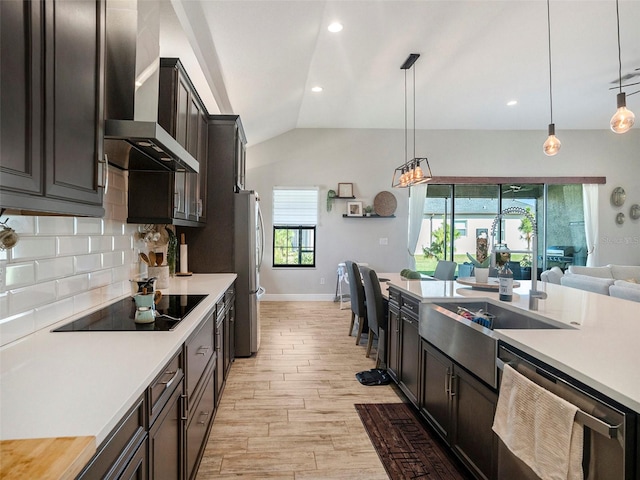 kitchen with light wood-type flooring, wall chimney range hood, appliances with stainless steel finishes, and hanging light fixtures