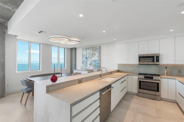 kitchen with white cabinetry, sink, kitchen peninsula, appliances with stainless steel finishes, and decorative backsplash