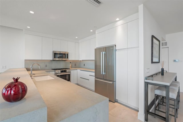 kitchen featuring stainless steel appliances, sink, kitchen peninsula, a kitchen breakfast bar, and white cabinets