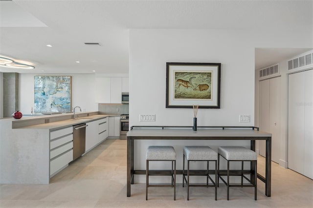 kitchen with a kitchen bar, decorative backsplash, sink, white cabinetry, and appliances with stainless steel finishes