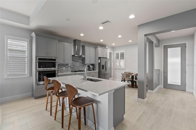 kitchen featuring gray cabinetry, appliances with stainless steel finishes, sink, a kitchen bar, and wall chimney exhaust hood