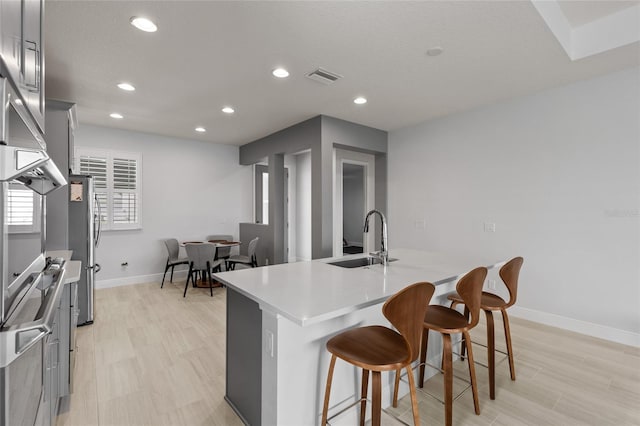 kitchen featuring an island with sink, a kitchen breakfast bar, light hardwood / wood-style flooring, gray cabinetry, and sink