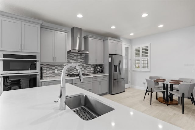 kitchen featuring wall chimney range hood, stainless steel appliances, light wood-type flooring, gray cabinets, and tasteful backsplash