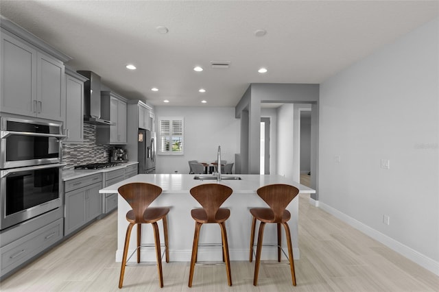 kitchen featuring wall chimney range hood, a kitchen bar, stainless steel appliances, gray cabinets, and sink